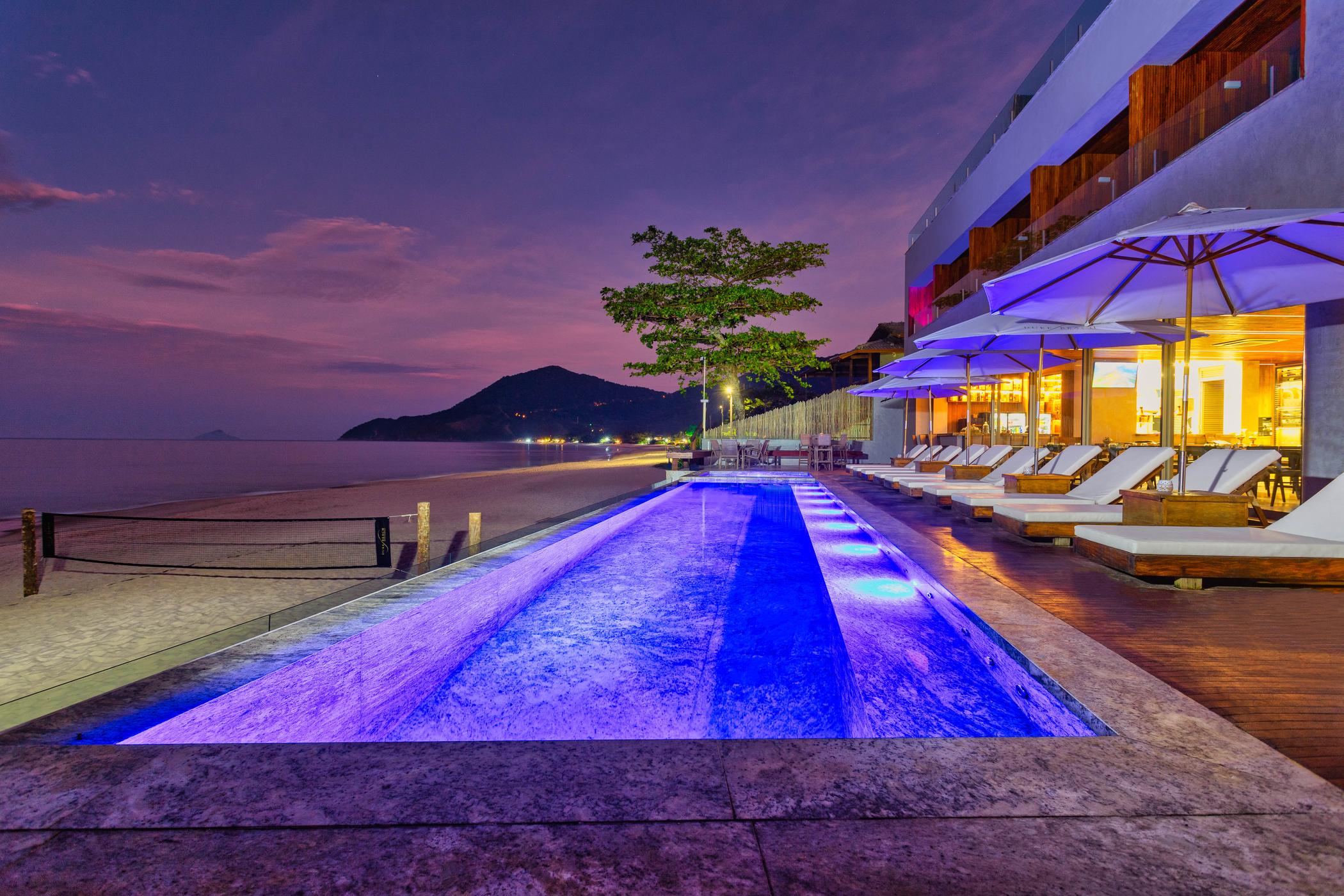 Der Infinity-Pool des Duke Beach in der Abenddämmerung, links der Strand von Maresias, rechts das beleuchtete Restaurant.